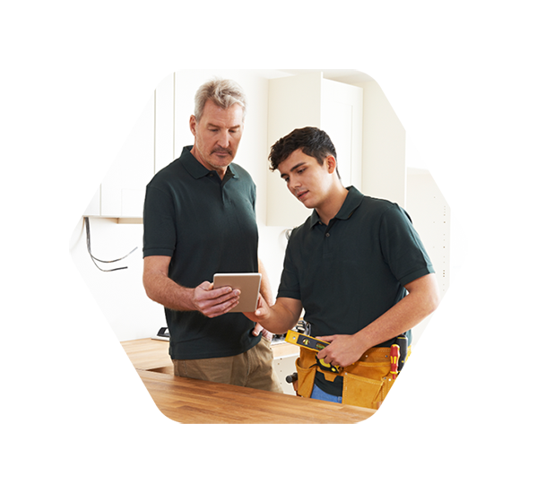 An installer and an apprentice reviewing kitchen installation details on a tablet, standing in a partially completed kitchen.