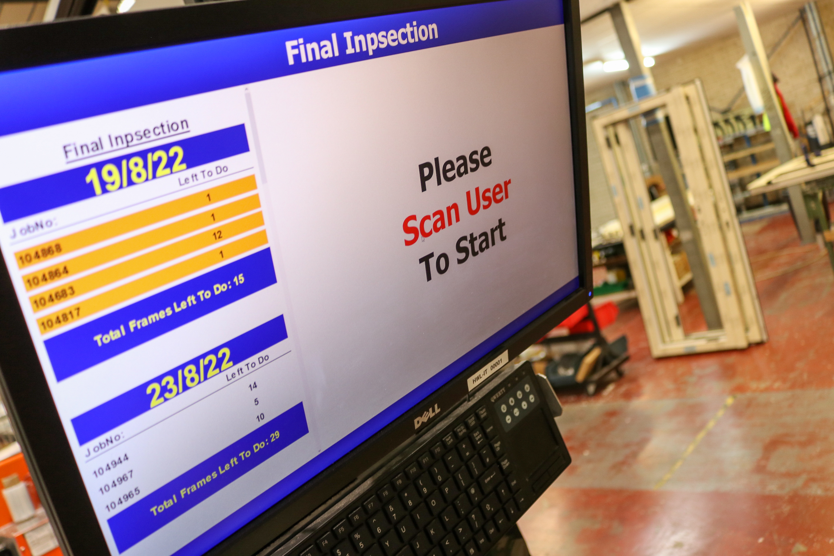 A computer screen displaying the "Final Inspection" interface, showing job numbers and tasks left to do for dates 19/8/22 and 23/8/22. The screen also displays a message instructing the user to scan to start. The background shows a workshop with equipment and materials.