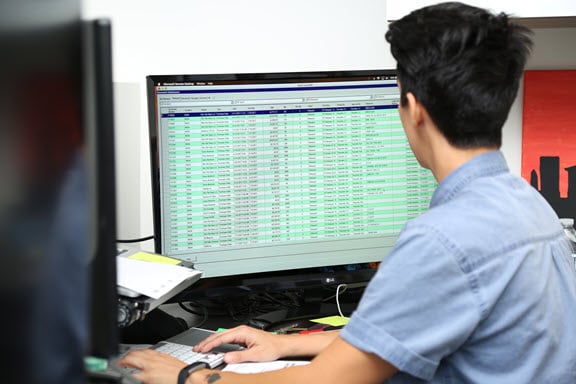 An Avanti employee working at a computer, analyzing data on a large monitor displaying detailed information in a tabular format, in a well-lit office environment.