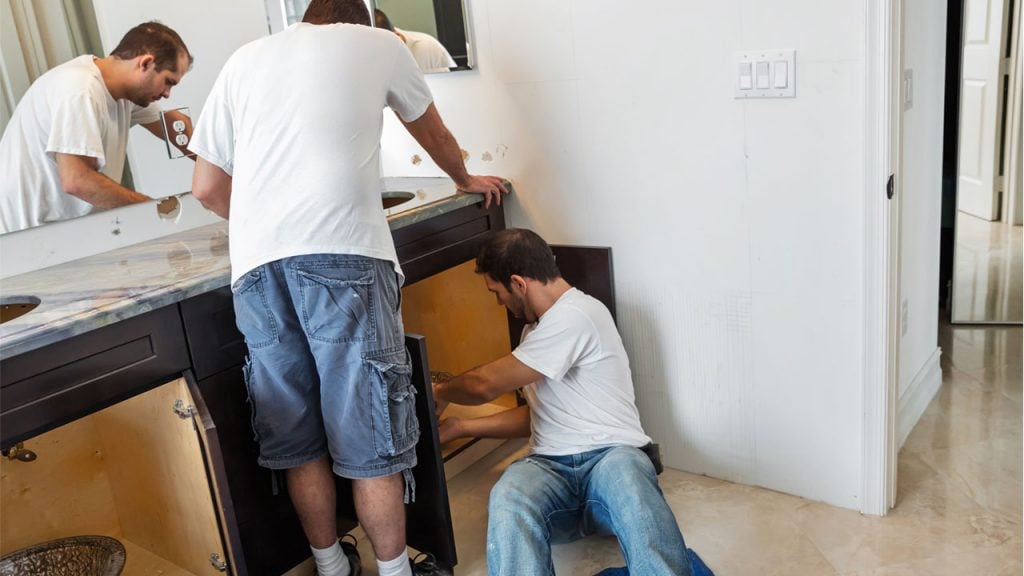 Two men installing a bathroom sink.