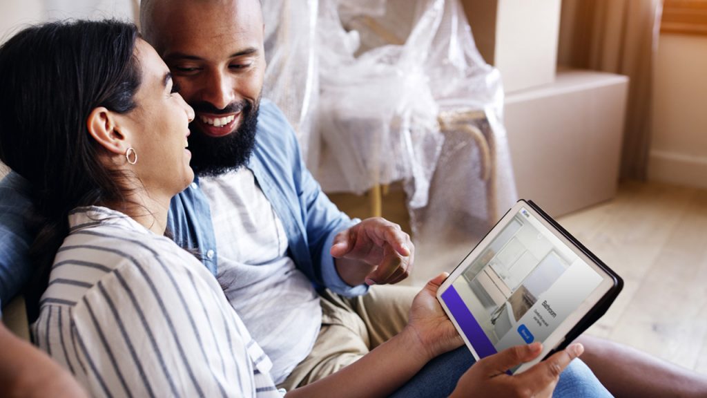 A man and woman sitting on a couch, looking at a tablet.