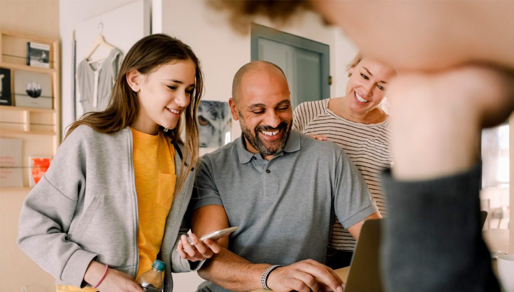 A family of four gathered around a laptop.