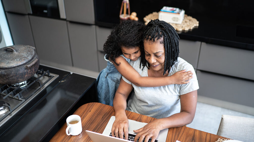 A woman and her daughter sitting at a table with a laptop.