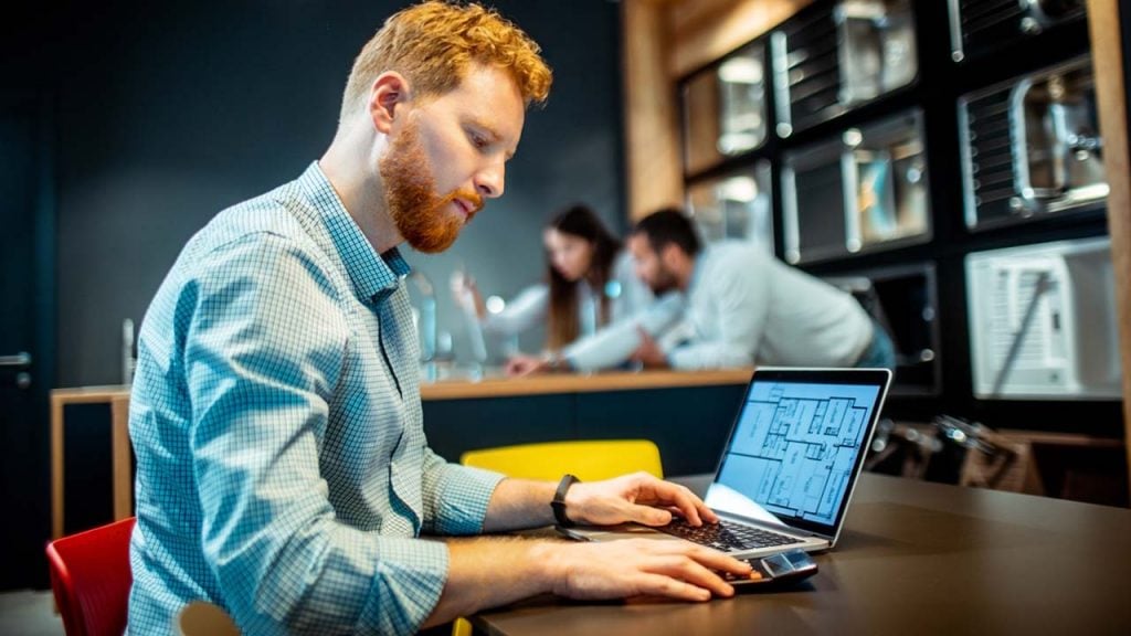 A man sitting at a table with a laptop, working on his computer.