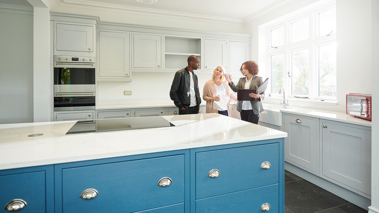 A couple standing in a kitchen with blue cabinets with a designer.