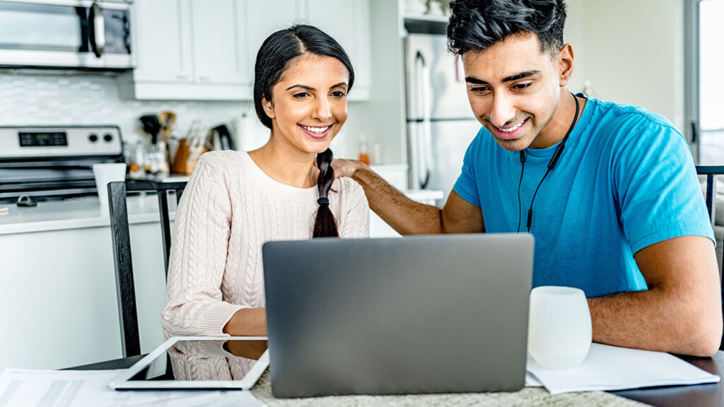 A couple sitting at a table with a laptop.