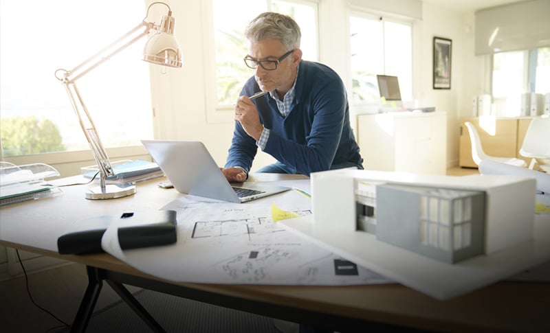 Designer working at desk with laptop and blueprints