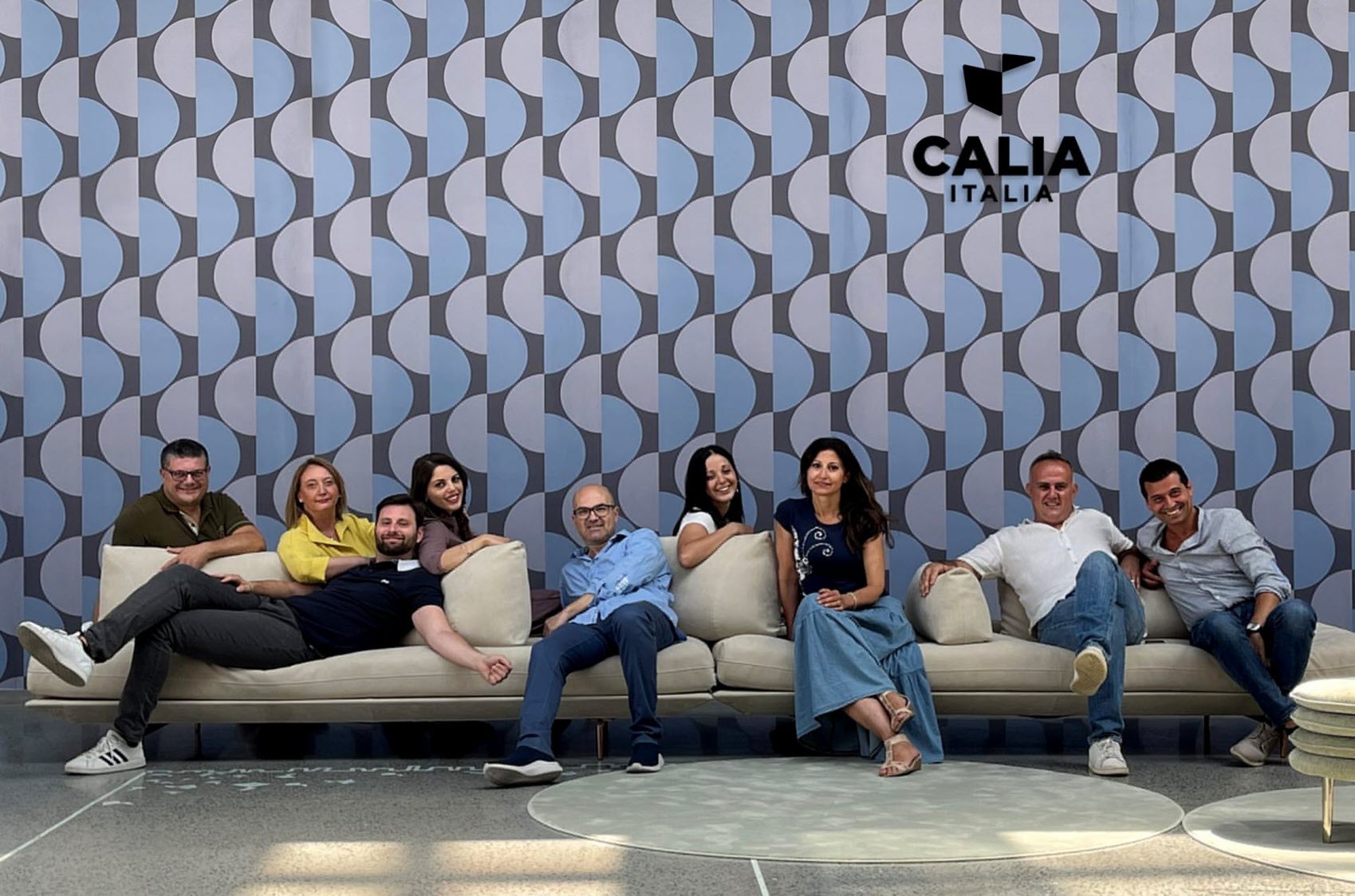 A group of eight Calia Italia staff sitting on a sofa in front of a wall with the Calia Italia logo.