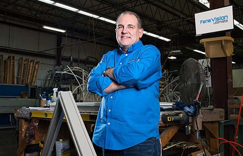 A man wearing a blue shirt stands confidently in a factory setting