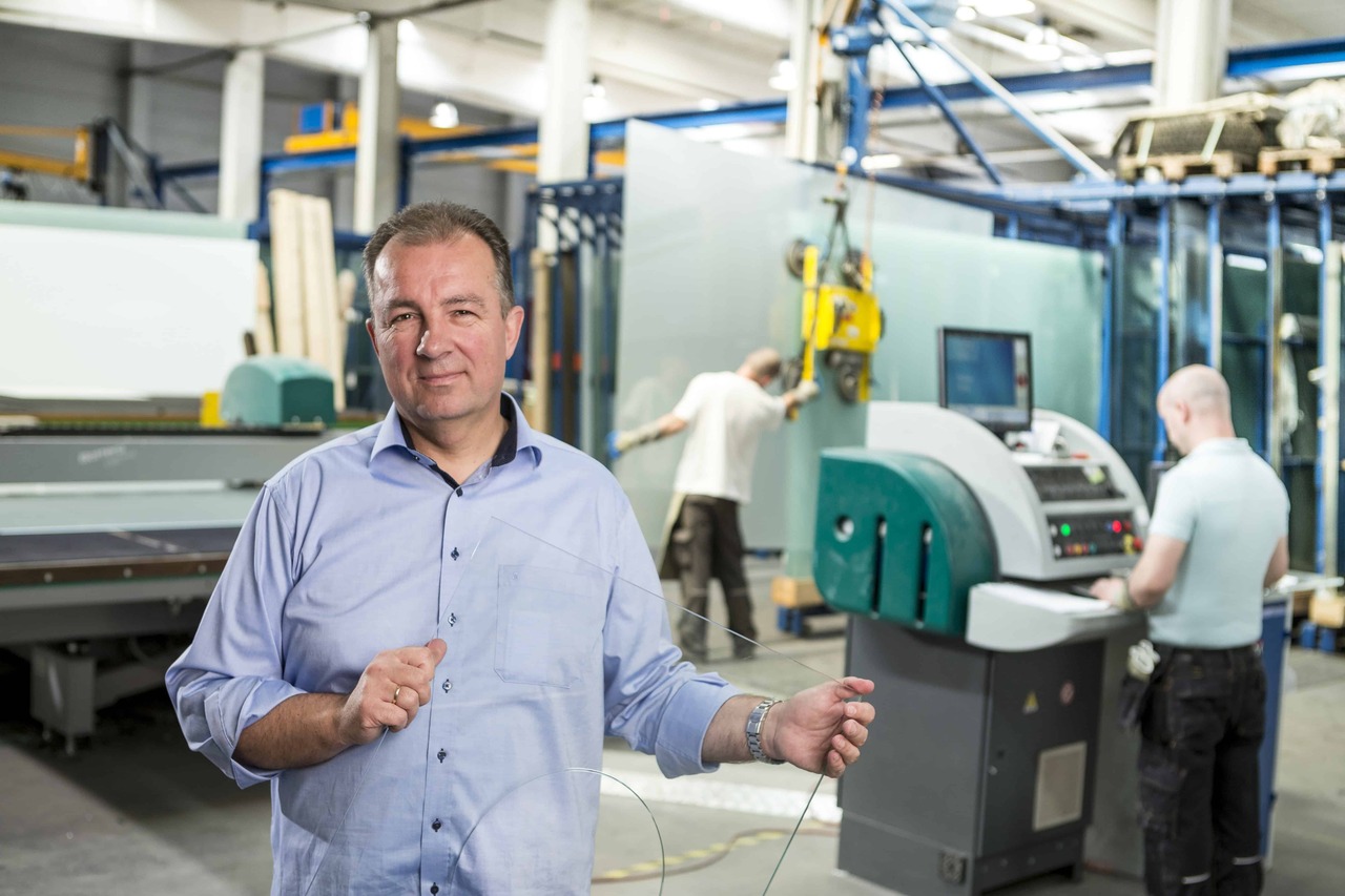 A man stands in front of a factory machine holding a sheet of glass