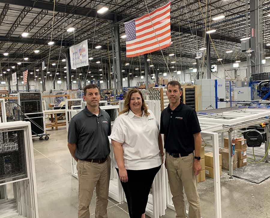 Three individuals stand before a large factory