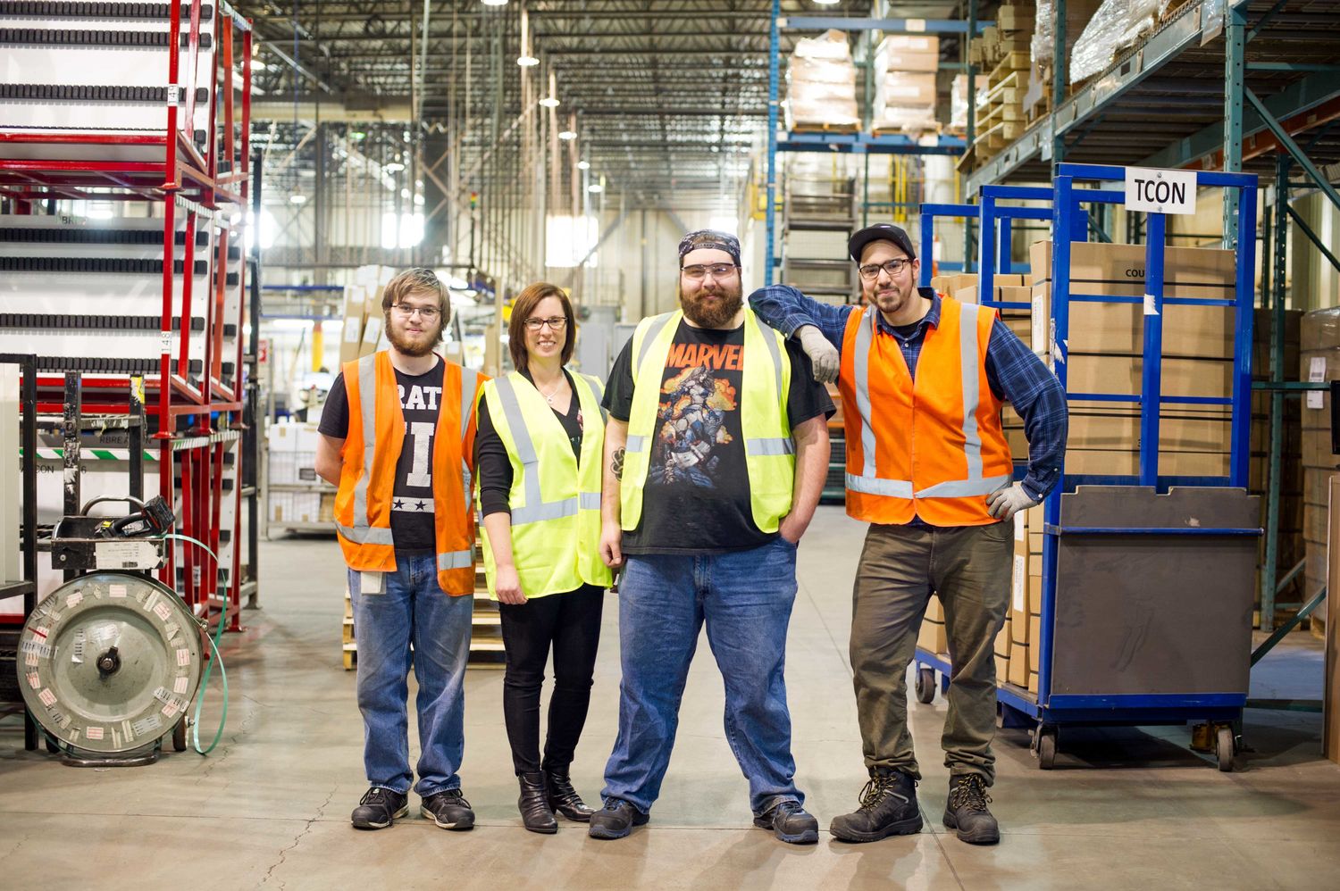 A group of four warehouse workers in high-visibility vests posing together in an industrial facility, symbolizing teamwork and workplace collaboration.