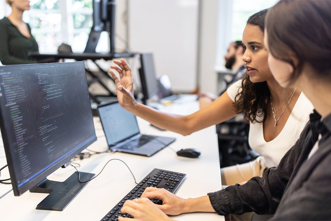 Two women working together at a computer in an office.