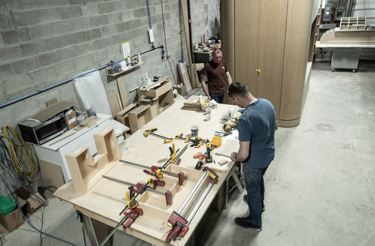 Two men collaborate on a wooden table in a workshop